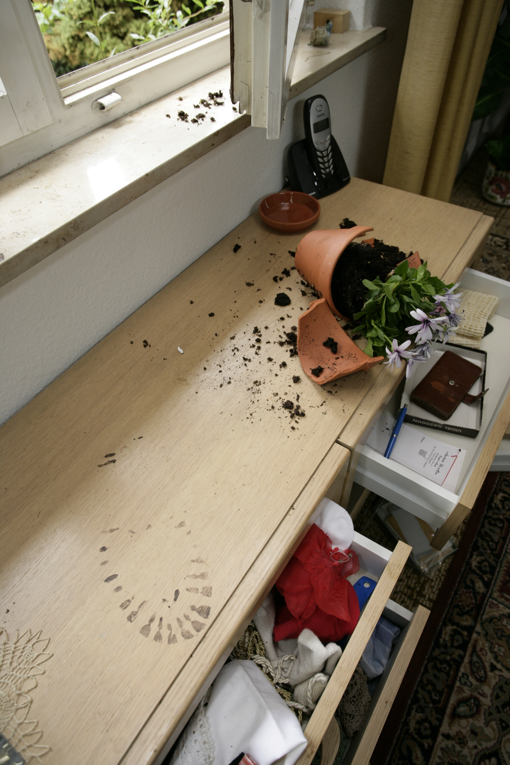 Spuren eines Einbruchs: aufgehebeltes Fenster, ein zerbrochener Blumentopf und werwüstete Schränke
