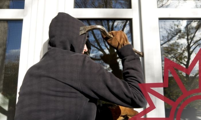 Mann mit Kapuze hebelt ein Fenster auf.